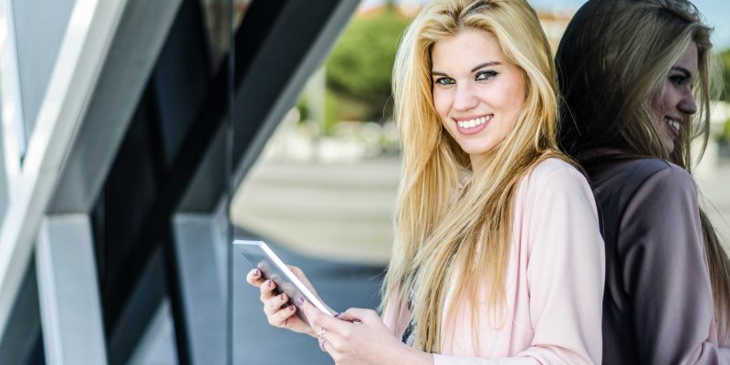 happy young blonde woman smiling with tablet on the street